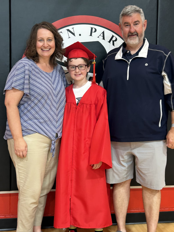 Two parents pose with their son at his elementary school graduation.