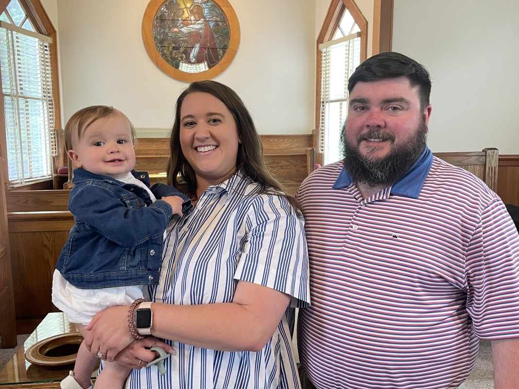Two parents smiling with their child in a church. The mother is holding the child.