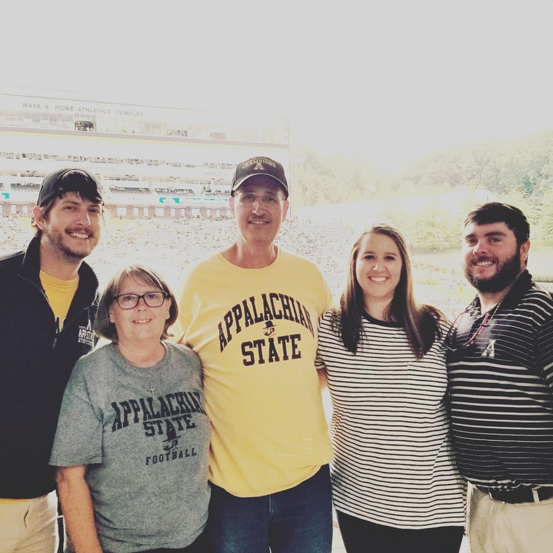 Five people standing side by side at an Appalachian State University football game.