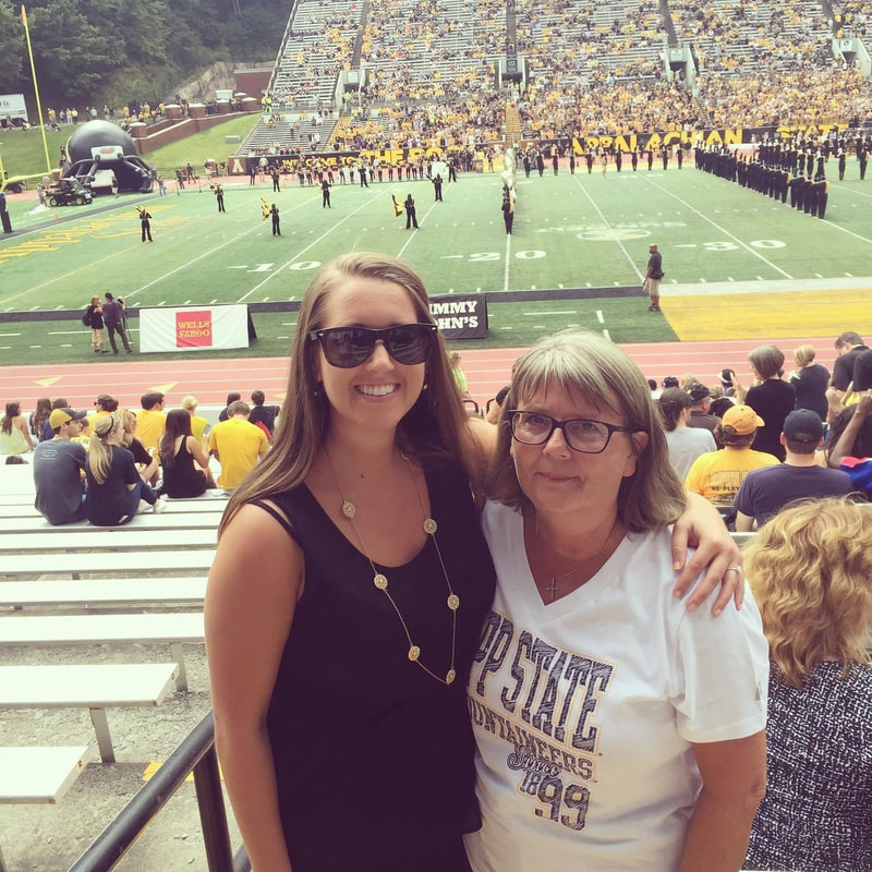 Two people standing together on the bleachers at an Appalachian State University football game.